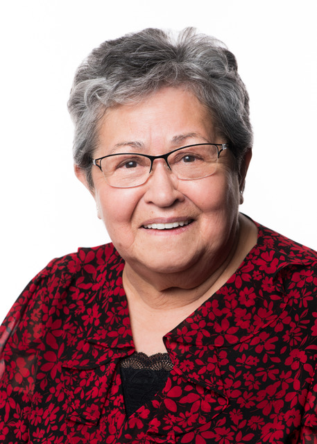 Smiling woman wearing glasses with short salt and pepper curly wearing a black blouse with red flower print